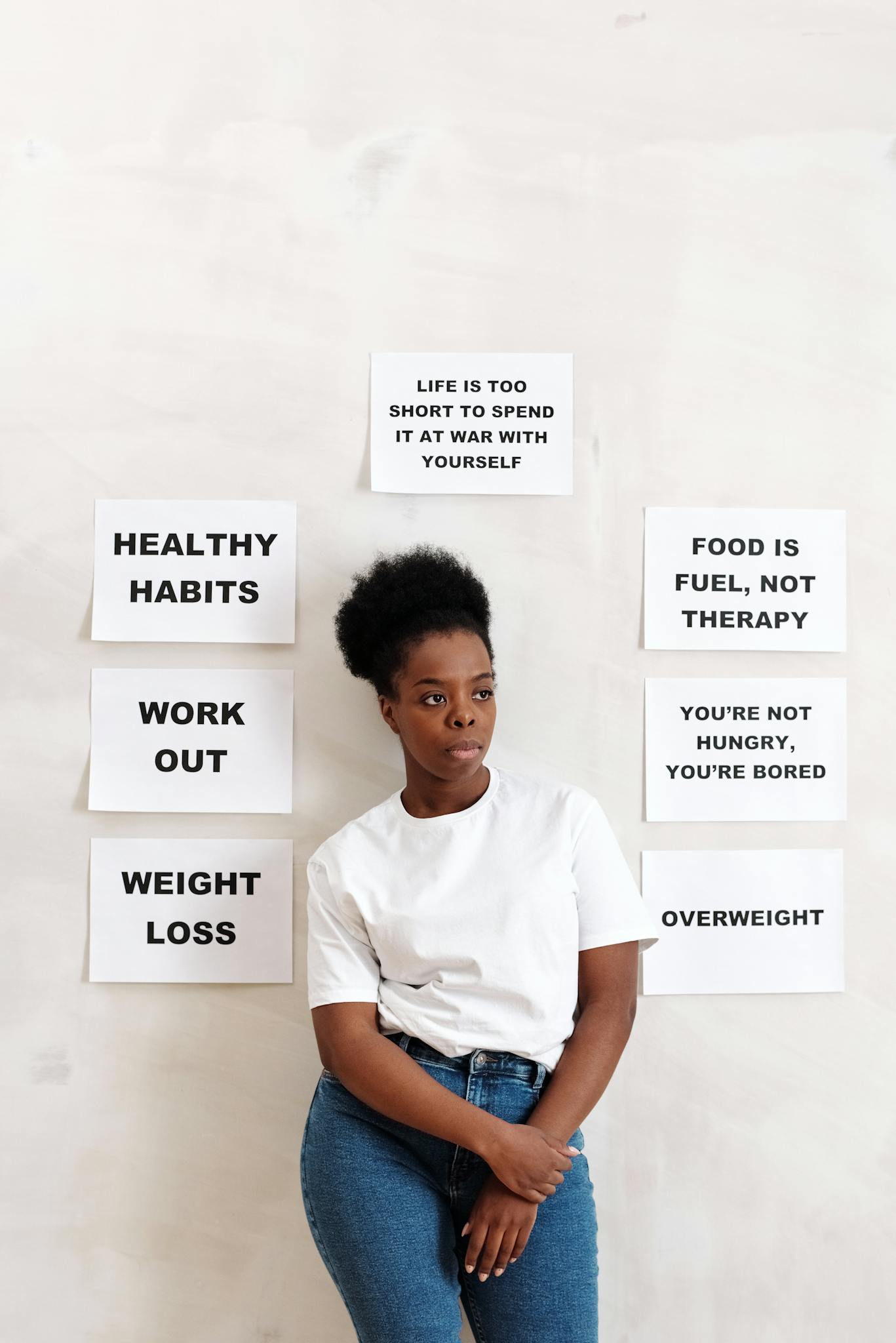 A woman stands by motivational self-care and wellness quotes on a wall.